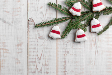 spruce branches and cookies shaped bell ring with red glaze on a white wooden background with copy space