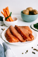 Marinated turkey steak with spices on a white plate  with carrot sticks and potato on the table.