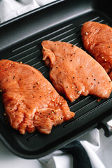 Marinated turkey steak with spices in a black grill pan on the table.