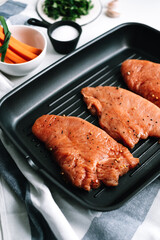 Marinated turkey steak with spices in a black grill pan on the table.