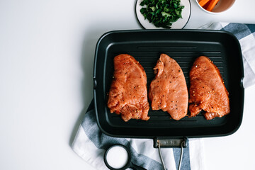 Marinated turkey steak with spices in a black grill pan on the table.