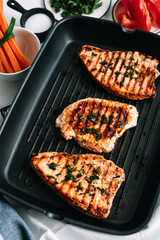 Grilled turkey steak with herbs and spices in black grill pan on the table.