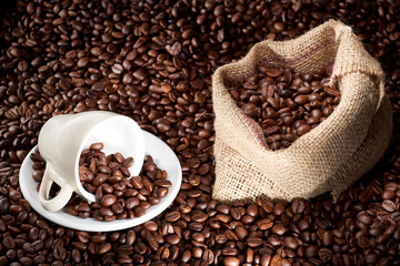 Studio Shot of White Cup of Coffee and Burlap Bag of Coffee over coffee beans and Cinnamon