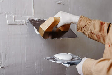 Close up of construction worker plastering and smoothing wall with trowel and putty knife. - obrazy, fototapety, plakaty