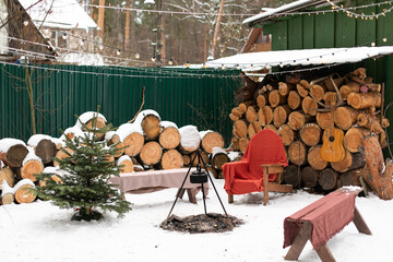 The campfire site is decorated with garlands. there are benches covered with blankets. Cuts of trees and firewood for a fire. Decorate your home for the holiday. Christmas in nature.