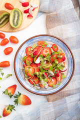 Vegetarian fruits and vegetables salad of strawberry, kiwi, tomatoes, microgreen sprouts on white concrete background. Top view, close up.