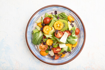 Vegetarian salad of pac choi cabbage, kiwi, tomatoes, kumquat, microgreen sprouts on a white concrete background. Top view, close up.