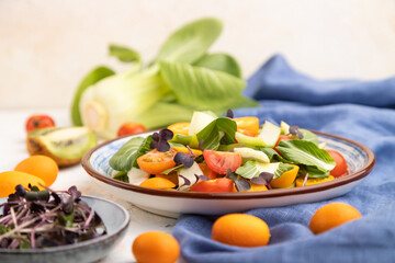 Vegetarian salad of pac choi cabbage, kiwi, tomatoes, kumquat, microgreen sprouts on a white concrete background. Side view, selective focus.