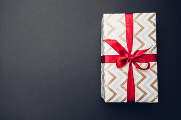Christmas and New year gift box wrapped in festive paper and decorated with red ribbon with bow on black background.