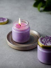 Aroma Candle. Lavender candle on a gray background. A match is set on fire with an aroma candle. Spring fragrance. Aromatherapy. Green in the background. Purple candle. Space for text. Spa.