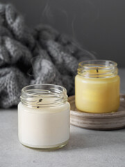 Burning candles on grey table, space for text. Grey knitted scarf and scented candles. Cozy winter atmosphere. 2021. Сolors of the year. burning candles on a gray background. New Year. Romantic.