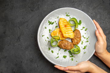 Hands holding tasty dinner with cutlet meal along with potatoes on a white plate on dark table