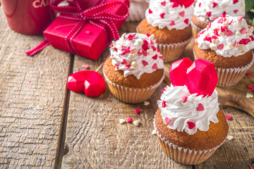 Cupcake with Heart for Valentines. Valentine Day Sweet Dessert, vanilla cupcakes with whipped vanilla cream and red sugar hearts decor for Valentine's Day, wooden background with rose flowers bouquet