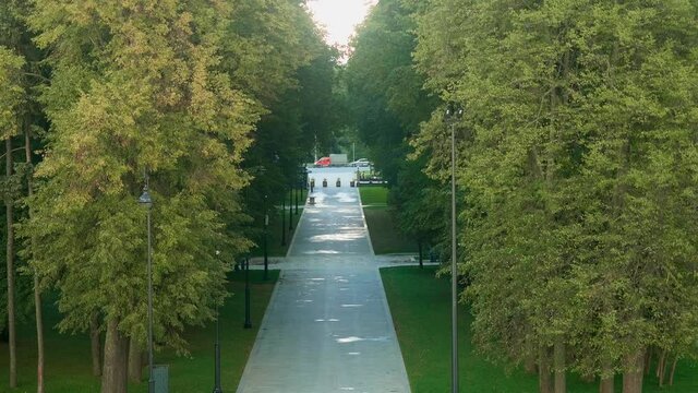 Up view of path leading to automobile road. Path is between rows of green trees. Coty park in Moscow