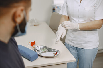 Skillful nurse is doing blood test for man in clinic. Man in a medical mask.