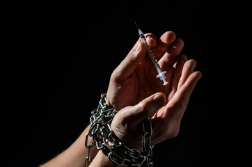 Human hands chained with a syringe for injection isolated on black background