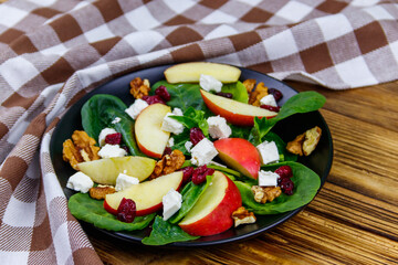 Autumn spinach salad with apple, feta cheese, walnut and dried cranberry on wooden table. Healthy vegetarian food