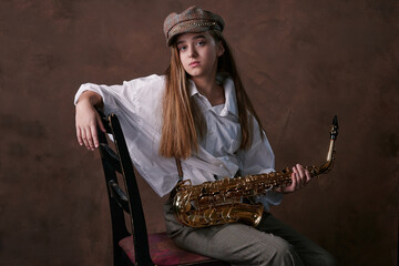 glamorous portrait of a girl with a saxophone. saxophonist with a musical wind instrument sits on a chair. studio. brown background