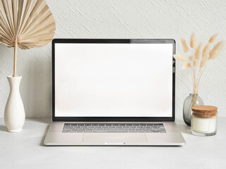 Laptop empty screen and different decoration against the white wall.