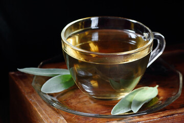 Sage herbal leaf tea or infusion in a glass cup with herb leaves nearby on wooden background, closeup, copy space, herbal drinks and naturopathy concept