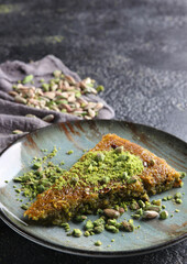 Oriental sweets. Pahlava with nuts, pistachio in a large dish on a black table. Turkish dessert. Background image, copy space, vertical