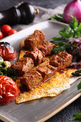 Turkish cuisine. Grilled meat on pita bread with grilled vegetables and herbs. Barbecue with salad on a grey plate with spices and a knife on a black table. Restaurant menu, vertical