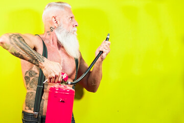 Fitness man showing his strength. Tattoo male model with white long beard in front of a yellow background. Calendar of a fireman. Elderly fitness and healthy concept.