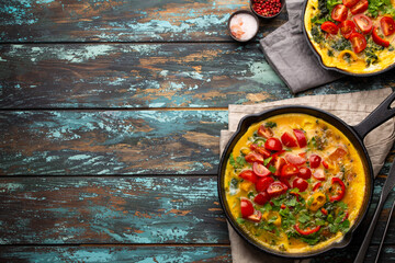 Healthy frittata in two cast iron pans with fried beaten eggs and seasonal vegetables on rustic...