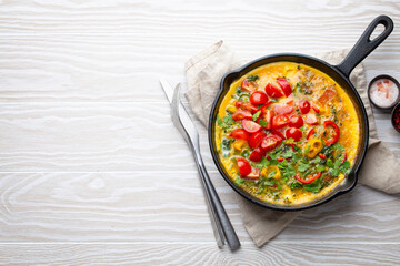 Healthy frittata in cast iron pan with fried beaten eggs and seasonal vegetables on white rustic...