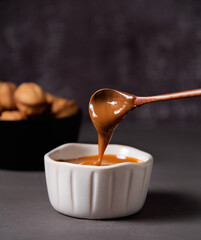 homemade caramel sauce flows from a spoon into a white bowl on dark backgroun