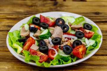 Tasty tuna salad with lettuce, black olives and fresh vegetables on wooden table