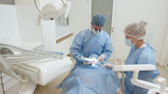 Two professional doctors doing dental surgery installing dental implants into patient's mouth in modern dental clinic hospital. Surgical operation. Stomatology. Treatment. Concept for dentistry.