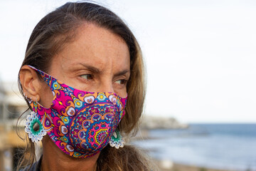Sad looking woman portrait wearing colorful face mask with mandala pattern and long huichol...