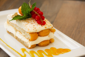 Succulent lady fingers cake with cream, red berries and glazed on top of white plate with peach jam...