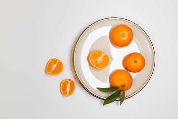 Fresh tangerine or clementin fruits on a beige plate with a gold rim on white background. Colorful fruit background. Flat lay, top view, copy space. Decorative christmas holiday composition.  