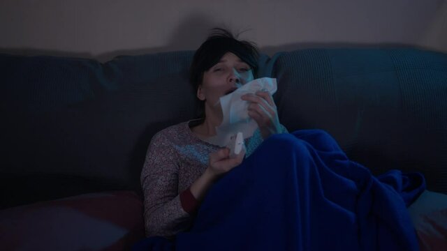 Young ill woman watching TV under the blanket. A sick day at home. Young ill woman infected by Coronavirus. Self-isolation.