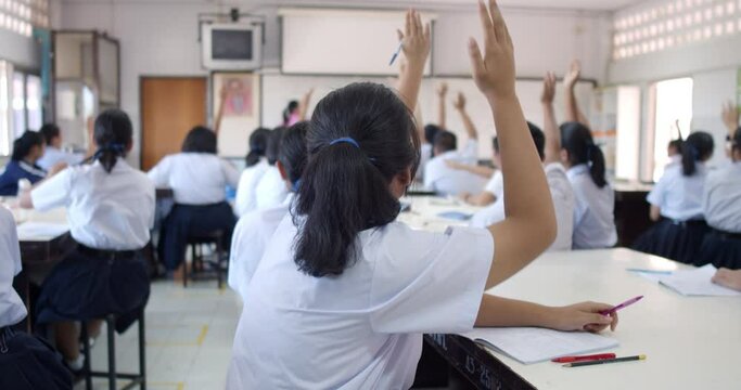 Slow motion of Asian high school students in white uniform actively study science by raising their hands to answer questions that teachers ask them  in classroom.