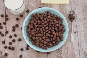 chocolate cereals in bowl and milk on wooden table.