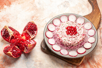 Above view of delicious chicken salad with beet on a gray plate on wooden cutting board and open pomegranate on mixed color background