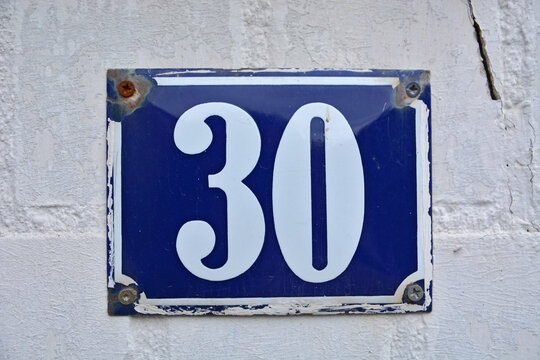 A blue house number plaque, showing the number thirty (30) 