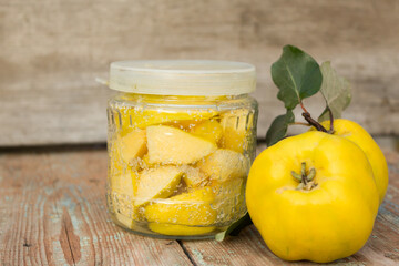 Ripe quince fruits on a wooden background. Candied quince slices in a glass jar. Conservation concept.