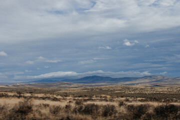 Beautiful autumn landscape with mountains on the horizon, dry grass, trees, roads, gardens, and fields, unusual great blue sky with  fluffy light gray clouds