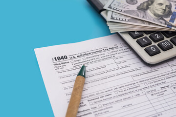 Tax concept. US tax form with calculator, pen and dollars on blue background. 1040 form for filling in April.