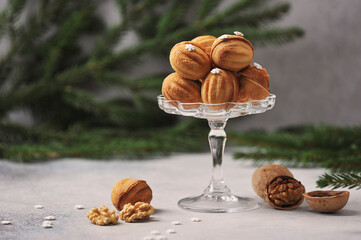 Nuts biscuits stuffed with boiled condensed milk.  Next to the vase are walnuts in shell and without shell.  Fir branches in the background.