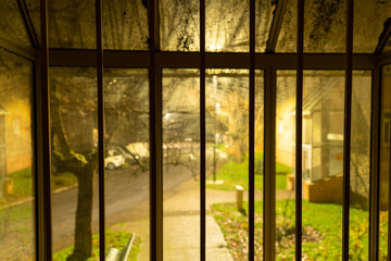 Dans une cage d'escalier, vue sur l'extérieur du quartier, de nuit: Fenêtre aux barreaux