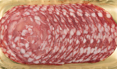 Thin slices of uncooked sausage on a golden backing. Food background.