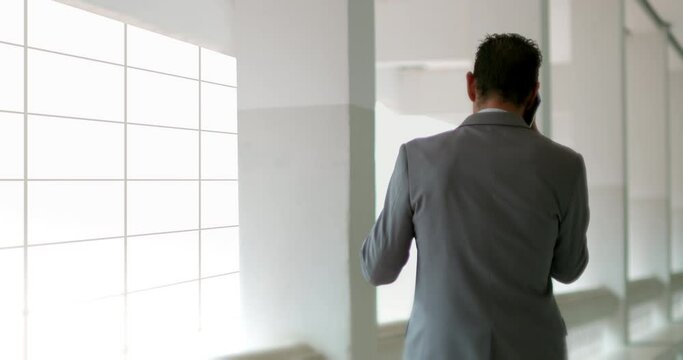 A funny business man in a suit and tie stands on the balcony outside his office room, talking on the mobile phone until receiving a successful result, very excited and dancing.