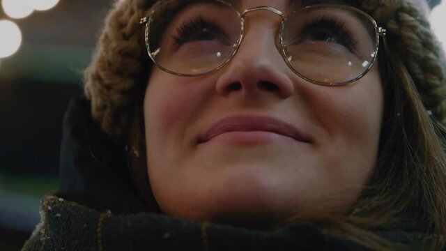 Close up face young attractive woman with glasses stand look around in winter Christmas time. Feel happy. Portrait. Outdoors. Pretty decoration street holiday. Slow motion
