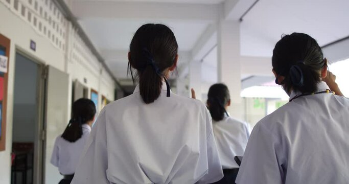 Slow motion scene and back view of female Asian high school students in a white uniform are walking on the corridor in the school building.