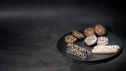 A pile of various cookies in a ceramic plate on a dark background. Place for your text. Dark photo of food.